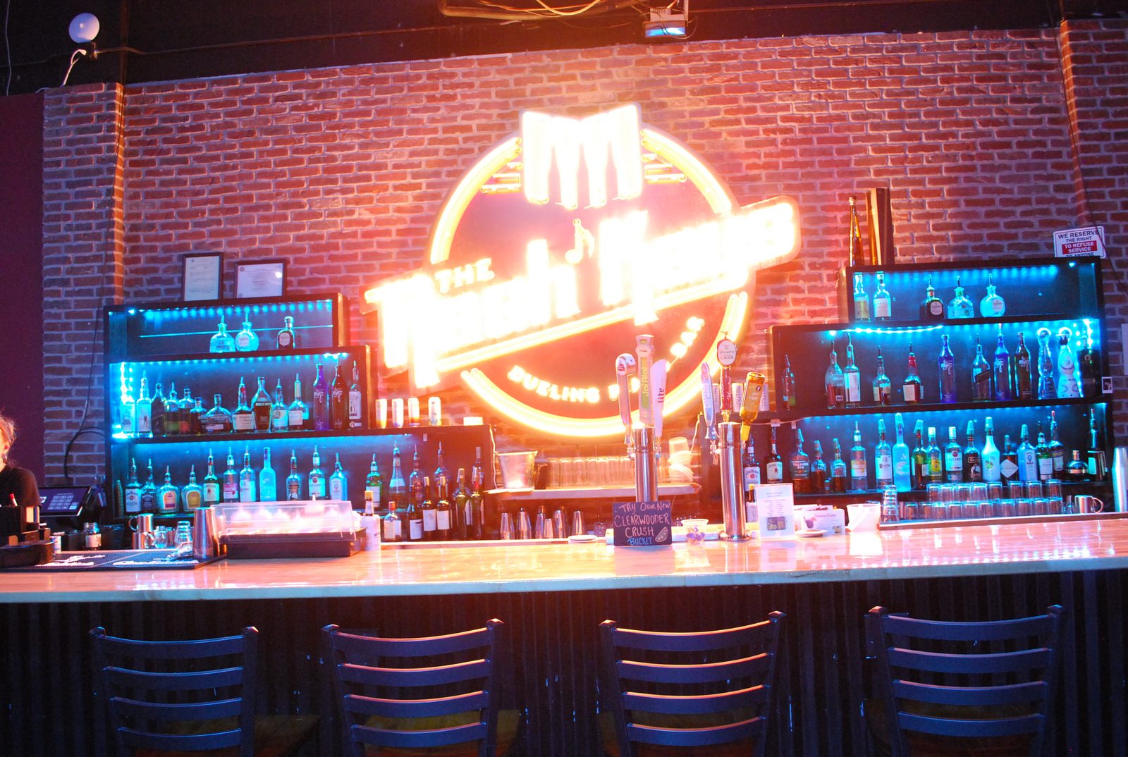 The full Nash Keys backbar — neon sign centered over lit bottle shelves and brick